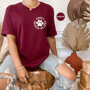 May include: A maroon t-shirt with a white paw print graphic and the text "Adopt. Foster. Rescue."