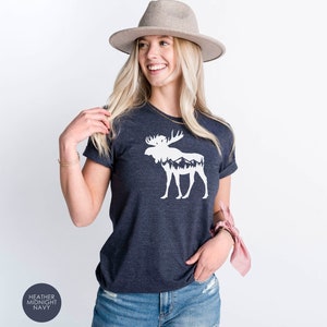 May include: Heather midnight navy t-shirt featuring a white moose graphic with mountain and forest details. The shirt has rolled sleeves and a crew neck. The text "Heather Midnight Navy" is in a circle in the lower left corner.