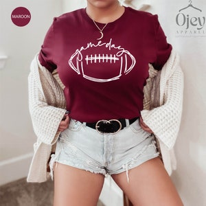 Peut inclure: Un t-shirt marron avec un graphique blanc d'un ballon de football et le texte "game day".