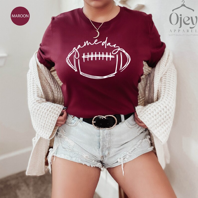 Peut inclure: Un t-shirt marron avec un graphique blanc d'un ballon de football et le texte "game day".