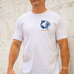May include: White crew neck t-shirt with a navy blue cougar head logo and the word "COUGARS" in gold. The logo is on the left chest. The shirt has short sleeves.