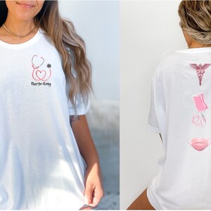May include: White t-shirt with a pink stethoscope, heart, and eye graphic on the front and the text "Nurse Day". The back of the shirt has a pink caduceus, syringe, and face mask graphic.