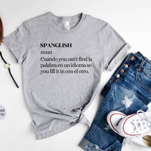 Puede incluir: Una camiseta gris jaspeada con la palabra "SPANGLISH" definida como "Cuando no encuentras la palabra en un idioma, la completas con el otro."