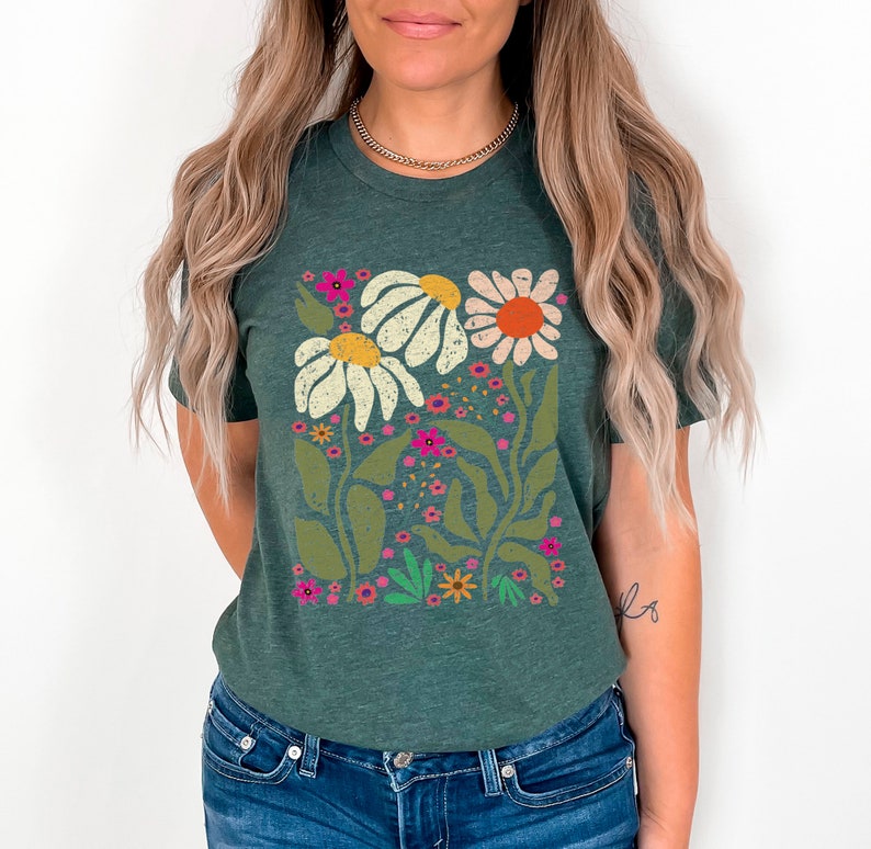 May include: A dark green t-shirt with a floral print featuring white, yellow, orange, pink, and green flowers. The flowers are stylized and have a retro feel.