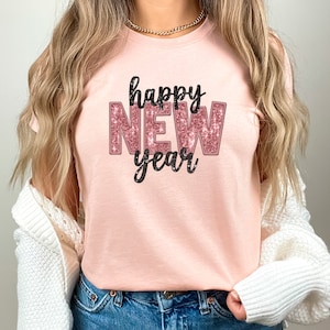 May include: A pink t-shirt with the text "happy new year" in black and pink glitter lettering.