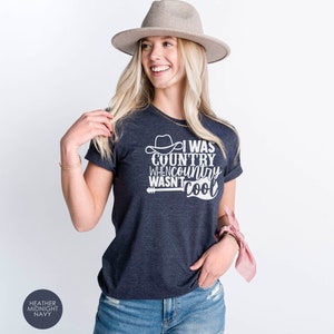 May include: A heather midnight navy t-shirt with a white graphic that says "I was country when country wasn't cool" with a cowboy hat and guitar graphic.