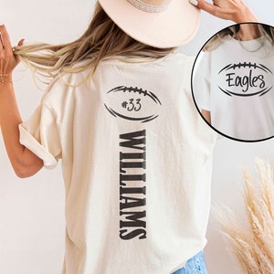 May include: White t-shirt with a black football graphic and the text "#33 WILLIAMS" on the back. The front of the shirt has a black football graphic with the text "Eagles".