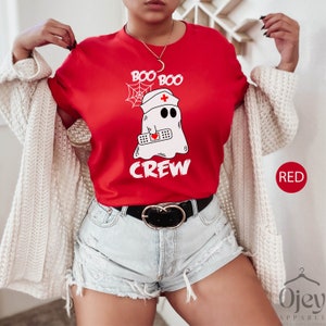 May include: Red t-shirt featuring a white ghost wearing a nurse's hat and holding a bandage. The text "Boo Boo Crew" is printed on the shirt.