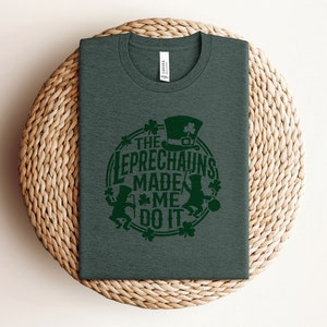 May include: A dark green t-shirt with a green shamrock design and the text "The Leprechauns Made Me Do It".