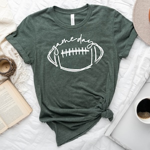 Peut inclure: Un t-shirt vert avec les mots "game day" et un contour blanc d'un ballon de football. Le t-shirt est nou&eacute; en bas.