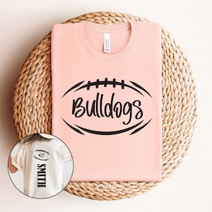 May include: A pink t-shirt featuring a black football graphic and the text "Bulldogs". A white t-shirt with the text "Smith #25" is also shown.