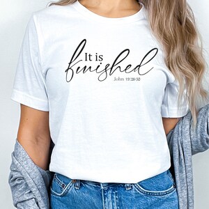 May include: White t-shirt with the text "It is finished" in black cursive lettering and the scripture reference "John 19:28-30" underneath.