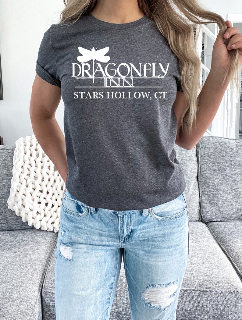 May include: A dark gray t-shirt with a white graphic of a dragonfly and the text "Dragonfly Inn Stars Hollow, CT".