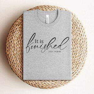 May include: A gray t-shirt with the text "It is finished" in black cursive lettering and the scripture reference "John 19:28-30" underneath.