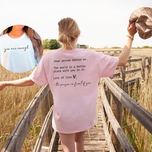 May include: A pink t-shirt with the text "Dear person behind me: The world is a better place with you in it. Lots of love - the person in front of you" printed on the back. A light blue t-shirt with the text "you are enough" printed on the front.