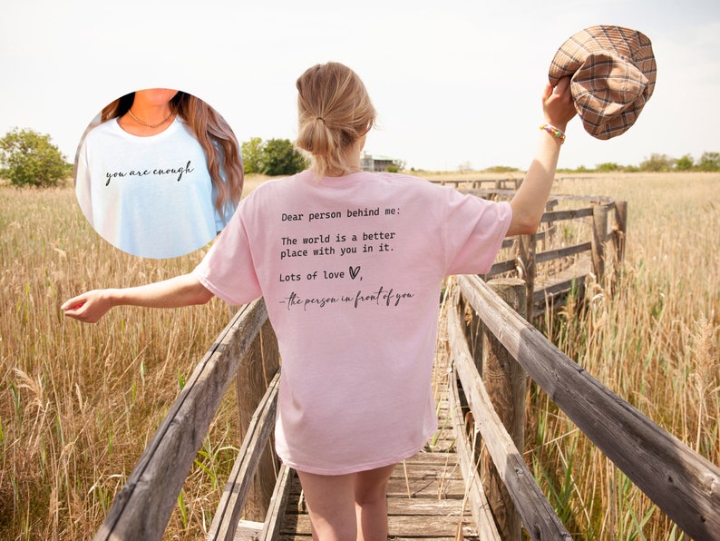 May include: A pink t-shirt with the text "Dear person behind me: The world is a better place with you in it. Lots of love - the person in front of you" printed on the back. A light blue t-shirt with the text "you are enough" printed on the front.