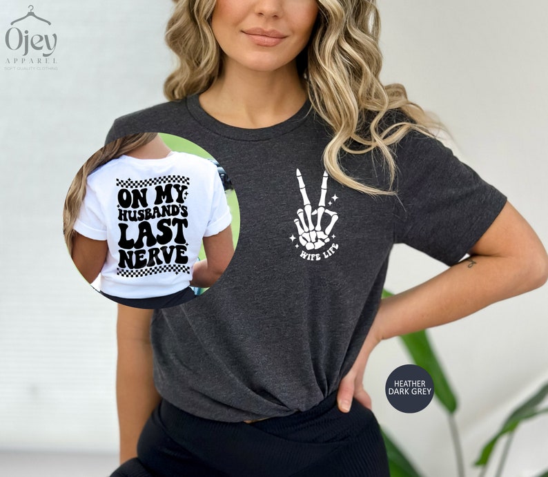 May include: A heather dark grey t-shirt with a skeleton hand making a peace sign and the text "Wife Life" on the front. The back of the shirt has the text "On My Husband's Last Nerve" in a retro font.