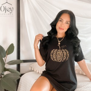 May include: Black t-shirt with a leopard print pumpkin graphic. The shirt is a loose fit and has short sleeves. The text "Ojev Apparel" is visible in the top left corner of the image.