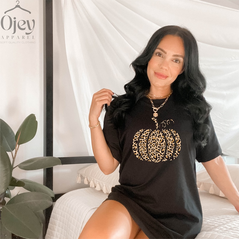 May include: Black t-shirt with a leopard print pumpkin graphic. The shirt is a loose fit and has short sleeves. The text "Ojev Apparel" is visible in the top left corner of the image.