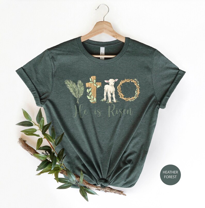 May include: A dark green t-shirt with a white lamb, a cross, a palm branch, and a crown of thorns. The text "He is Risen" is printed below the image.