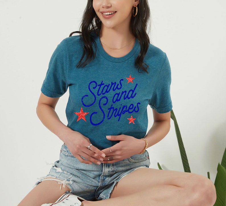 May include: A teal blue t-shirt with the text "Stars and Stripes" in blue script with red glitter stars.
