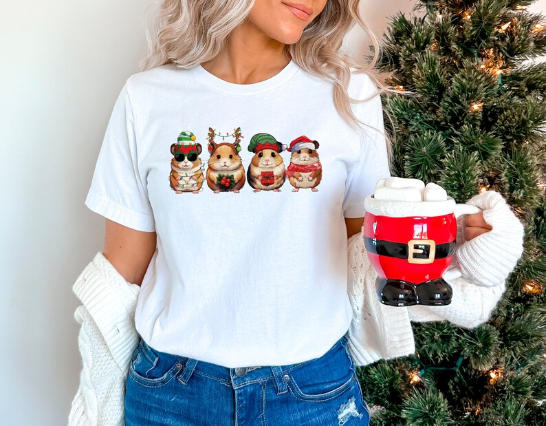May include: White t-shirt with a graphic of four hamsters wearing Christmas hats and holding gifts. The hamsters are wearing a Santa hat, an elf hat, a reindeer hat, and a snowman hat.