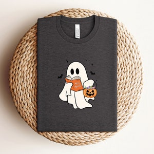 May include: A dark gray t-shirt with a white ghost holding a book that says "Scary Stories" and a pumpkin bucket with candy.