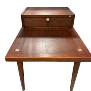 May include: A mid-century modern wooden side table with a drawer and a lower shelf. The table has a rich brown finish, tapered legs, and a silver-toned drawer pull. Decorative X-shaped inlays are on the tabletop.