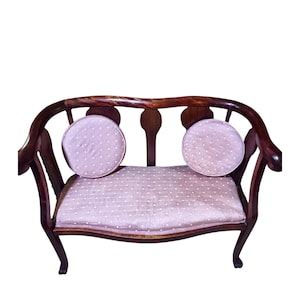 May include: A vintage loveseat with a dark wood frame and curved back. The seat and two round back cushions are upholstered in a light pink fabric with a white polka dot pattern. The loveseat has curved legs.