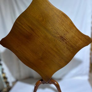 May include: A wooden side table with a unique, diamond-shaped top. The table is made of a warm-toned wood, with a three-legged base. The table's top measures approximately 30 inches across, and the legs are curved.