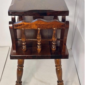 May include: A dark brown wooden side table featuring a rectangular top, a lower shelf, and four turned legs. The middle section includes a decorative spindle gallery with three vertical balusters and a scalloped top rail for storage.