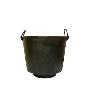 Puede incluir: Un cubo de metal verde oscuro con dos asas arqueadas. El cubo tiene una base ancha y redondeada y una parte superior ligeramente ensanchada. El metal tiene un aspecto texturizado y envejecido, lo que sugiere que es vintage o antiguo.