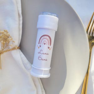 Peut inclure: Une baguette à bulles en plastique blanche avec un motif arc-en-ciel rose et brun et le nom "Luna Gans" imprimé sur le devant.