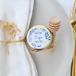 May include: A small jar of honey with a gold lid and a blue and yellow floral label that says "BAPTÊME Ezjo 04.01.2025". A wooden honey dipper is attached to the jar with twine.