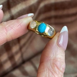 K&ouml;nnte beinhalten: Ein goldener Ring mit drei ovalen Edelsteinen. Der mittlere Stein ist t&uuml;rkisblau, die beiden Steine an den Seiten sind wei&szlig;.