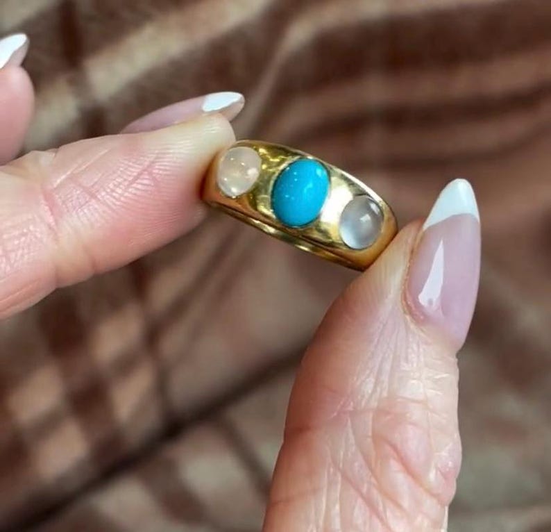 K&ouml;nnte beinhalten: Ein goldener Ring mit drei ovalen Edelsteinen. Der mittlere Stein ist t&uuml;rkisblau, die beiden Steine an den Seiten sind wei&szlig;.
