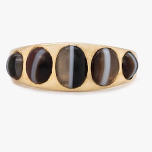 Può includere: Un anello d'oro con cinque pietre di agata ovali incastonate in una fascia. Le pietre sono nere, bianche e marroni con un motivo a strisce.