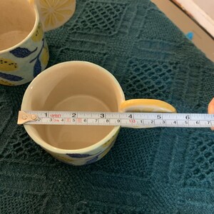 Pode incluir: Caneca de cer&acirc;mica com al&ccedil;a de fatia de lim&atilde;o e padr&atilde;o de folhas de lim&atilde;o e azuis. A caneca tem aproximadamente 7,6 cm de di&acirc;metro. O interior &eacute; creme.