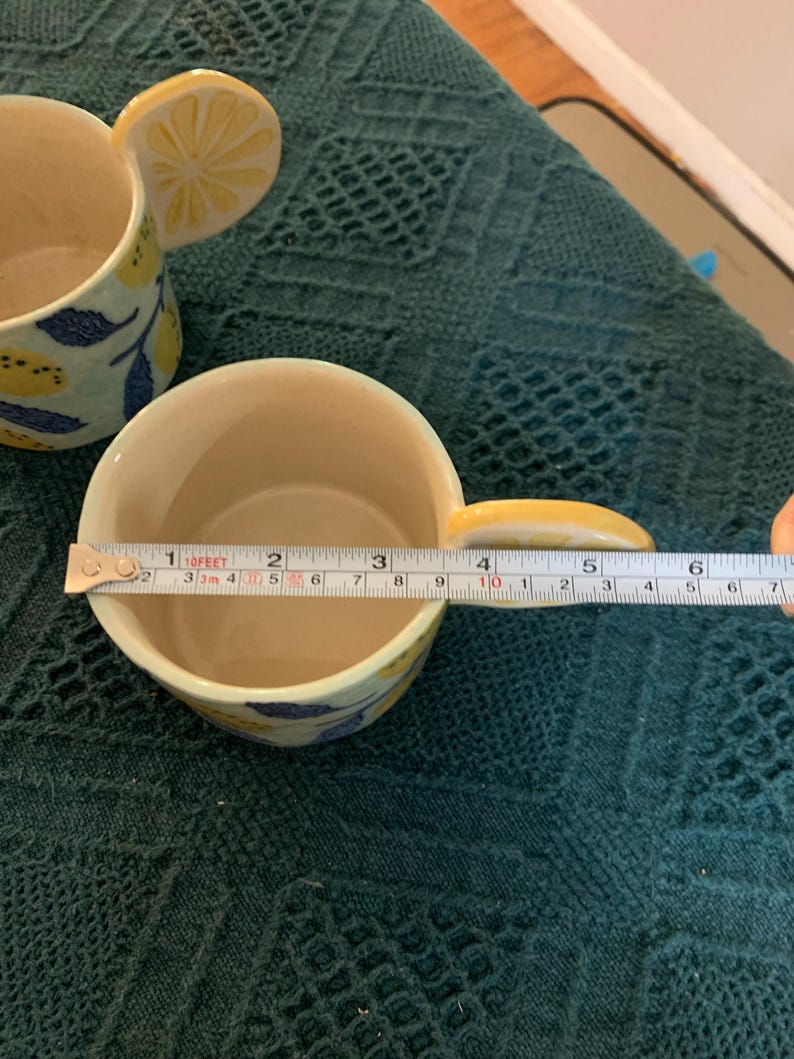 Pode incluir: Caneca de cer&acirc;mica com al&ccedil;a de fatia de lim&atilde;o e padr&atilde;o de folhas de lim&atilde;o e azuis. A caneca tem aproximadamente 7,6 cm de di&acirc;metro. O interior &eacute; creme.