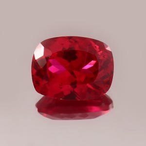 Op de afbeelding: Een dieprode edelsteen met een kussen-slijpvorm. De edelsteen is gefacetteerd en heeft een hoge glans.