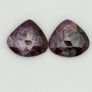 May include: Two pear-shaped faceted gemstones with a purple and grey colour.