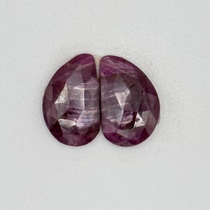 May include: Two pink pear-shaped gemstones with a faceted cut.