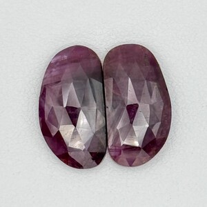 May include: Two faceted, oval-shaped, pink gemstones with a light purple hue.