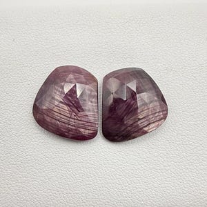 May include: Two faceted, purple-hued gemstones with a starburst pattern. The stones are cut in a unique, geometric shape.