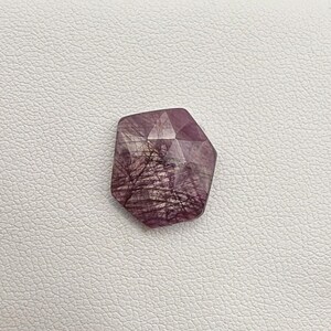 May include: A faceted, pink and white gemstone with a starburst pattern. The gemstone is cut in a hexagonal shape.
