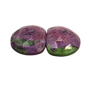 May include: Two oval-shaped gemstones with a green and purple colour pattern. The stones are faceted and have a glossy finish.