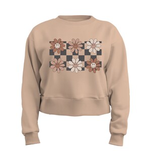 May include: A beige cropped sweatshirt with a checkered pattern featuring six smiling flower designs in shades of brown, pink, and white.