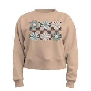 May include: A beige cropped sweatshirt with a checkered pattern and six pastel green, blue, and pink flowers with smiley faces.