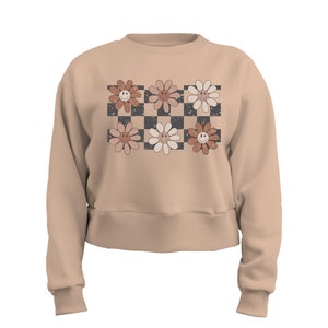 May include: A beige cropped sweatshirt with a checkered pattern and six smiling flower designs in shades of brown, pink, and white.