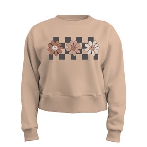 May include: A beige cropped sweatshirt with a checkered pattern and three smiling flower designs in shades of brown, pink, and white.